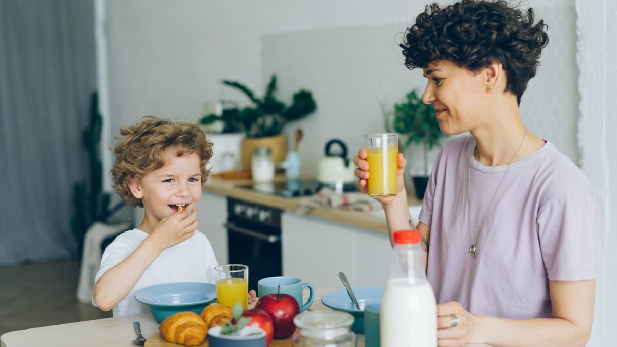 Mother and son sharing a joyful breakfast at home. Smiling and bonding over food and drinks.